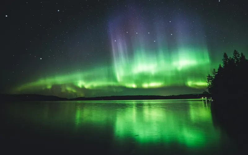 Noorderlicht weerspiegeld in een rustig meer met herfstberken