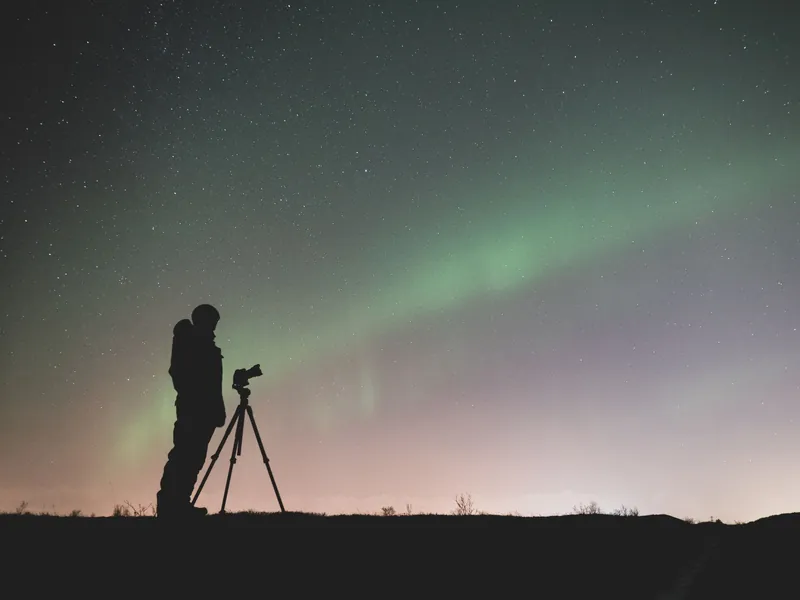 Fotograaf naast een statief onder zwak noorderlicht